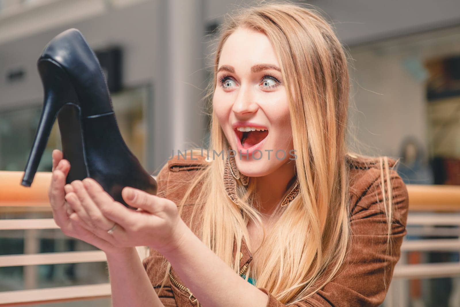 Woman holding shoe. Women loves shoes concept. Blonde girl and black high heels shoes on the background of mall. surprise and delight