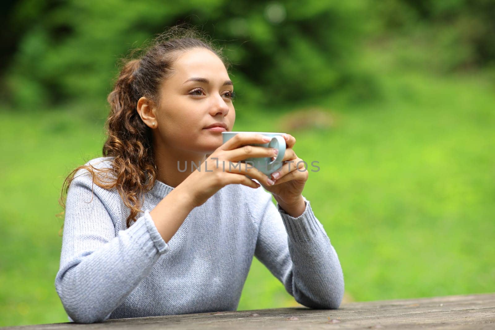 Distracted woman in a park drinking coffee looking away