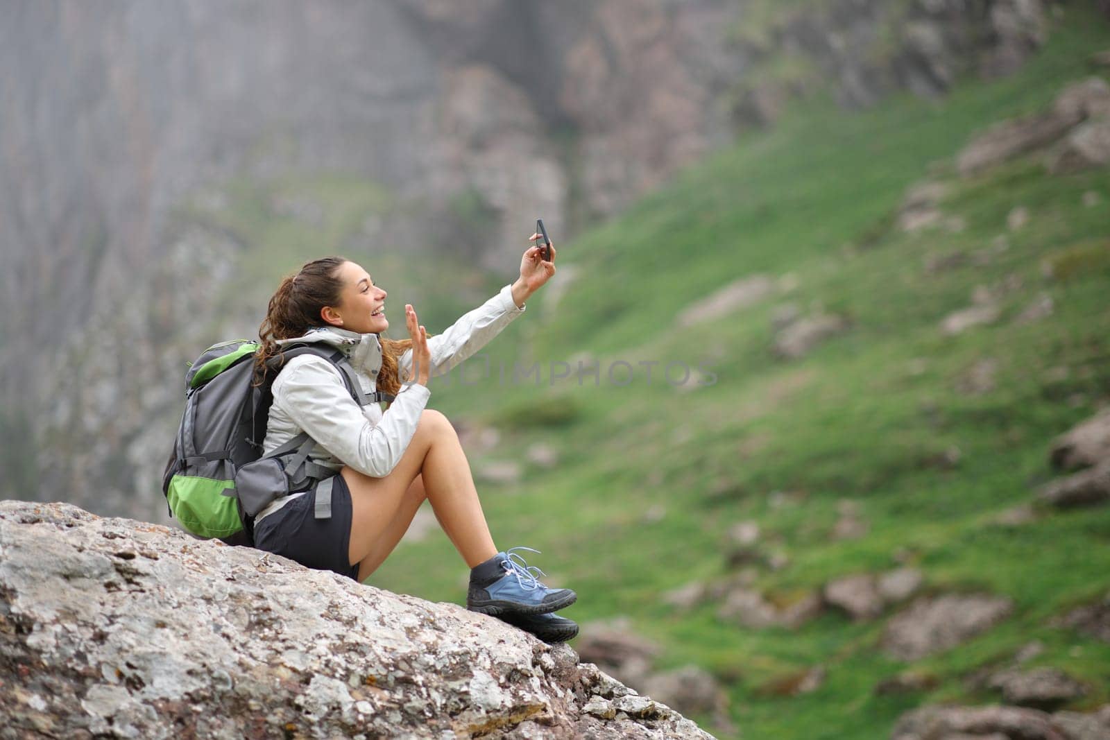 Happy hiker taking selfie with smart phone on a rock in the mountain
