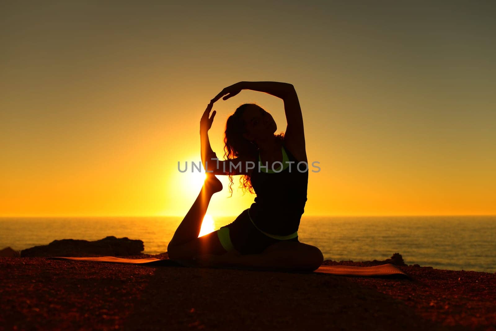 Backlights yogi silhouette at sunset doing yoga exercise on the beach