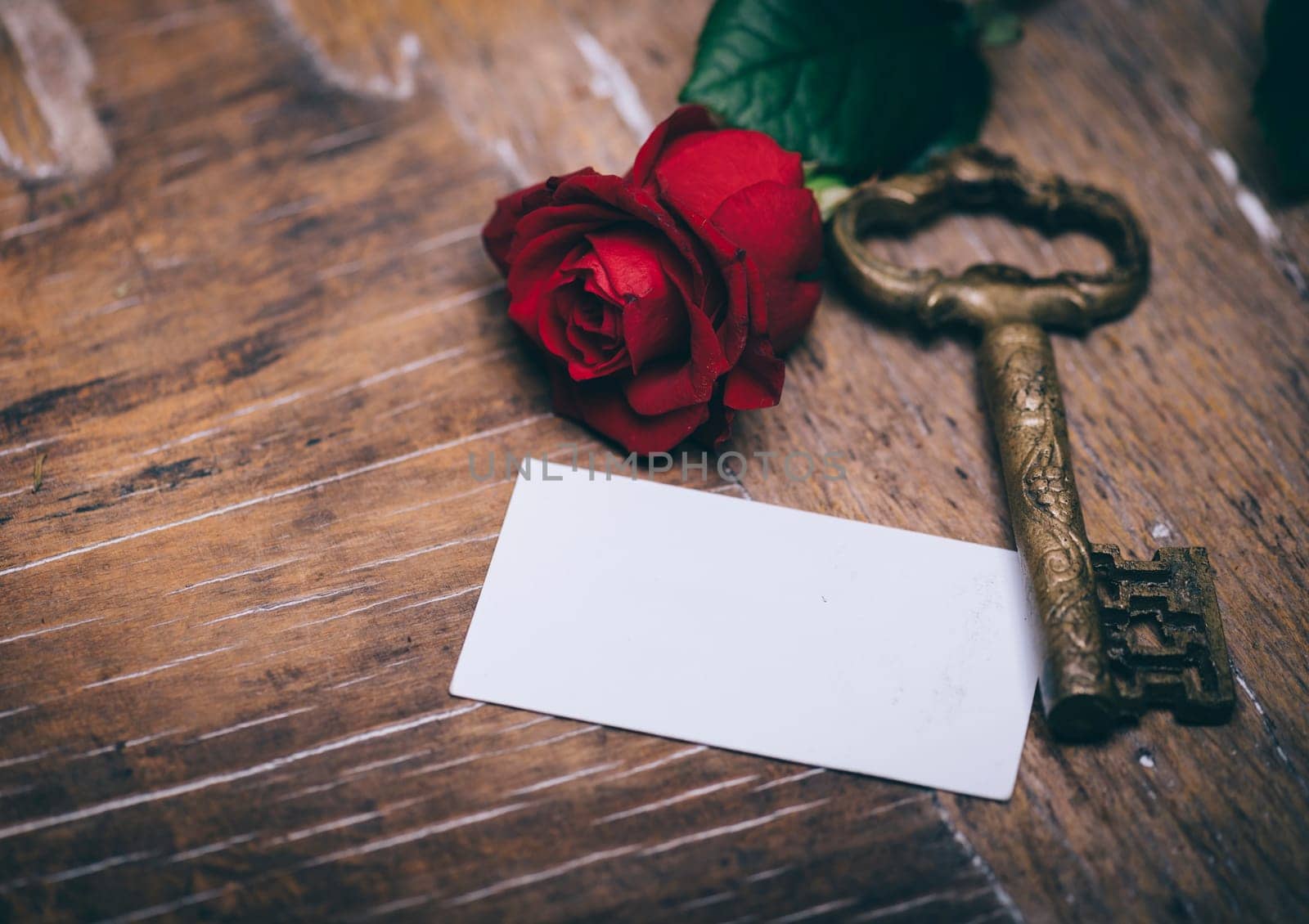 Valentine's day still life concept. Valentine gift, red rose, vintage key and empty greeting card on wooden table. Valentine holiday design.