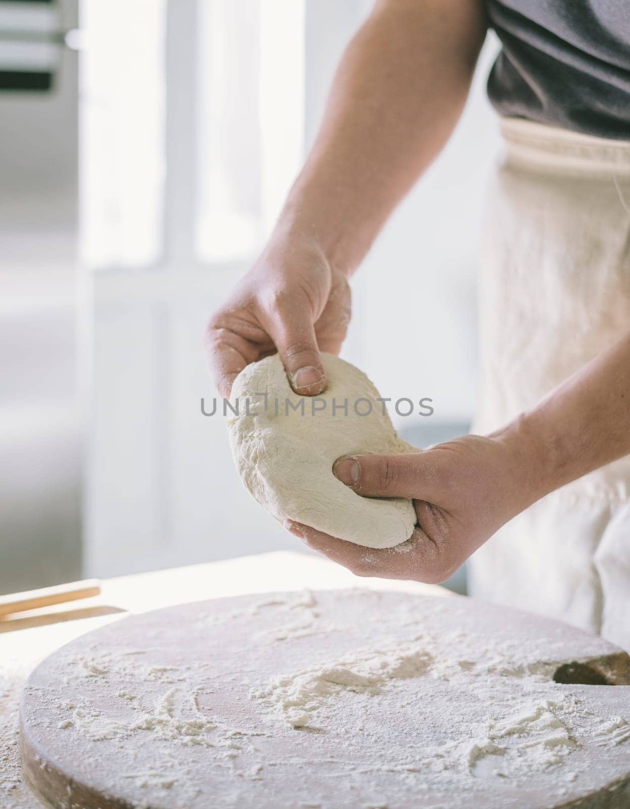 Man kneading dough and baking homemade pastry in the kitchen. Closeup on baker's hands preparing loaf of bread. Cooking and food preparation at home.