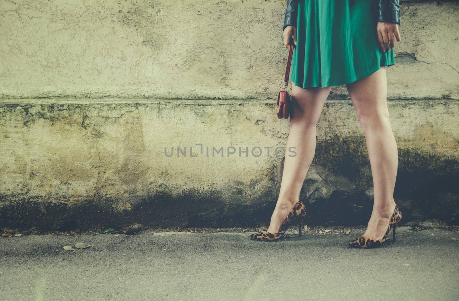 Sexy female legs in modern high heels walking on the street. Woman in front of street wall in fashionable leopard pattern print high heel shoes. Retro style filter with copyspace background.