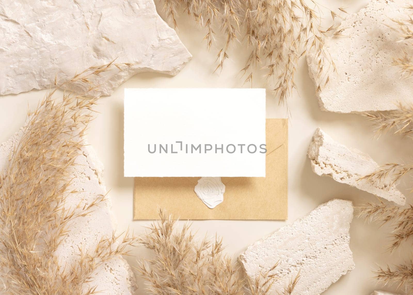 Blank card and enveelope near beige travertine stones and dried pampas grass top view, mockup. Boho scene with horizontal card. Bohemian or close to nature greeting or wedding Invitation.