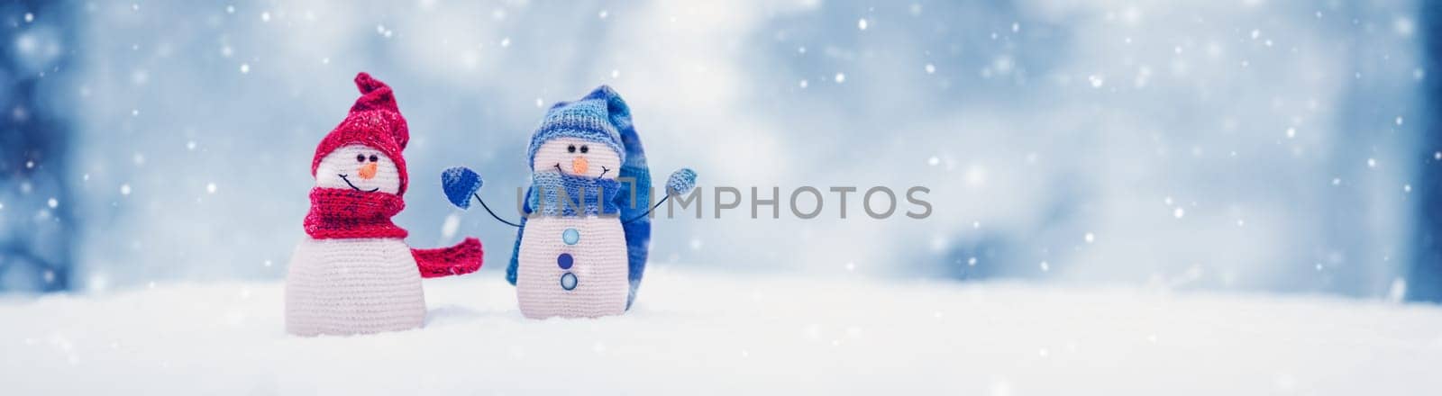 Little knitted snowmen on the white snow on blue background. Beautiful panoramic view.