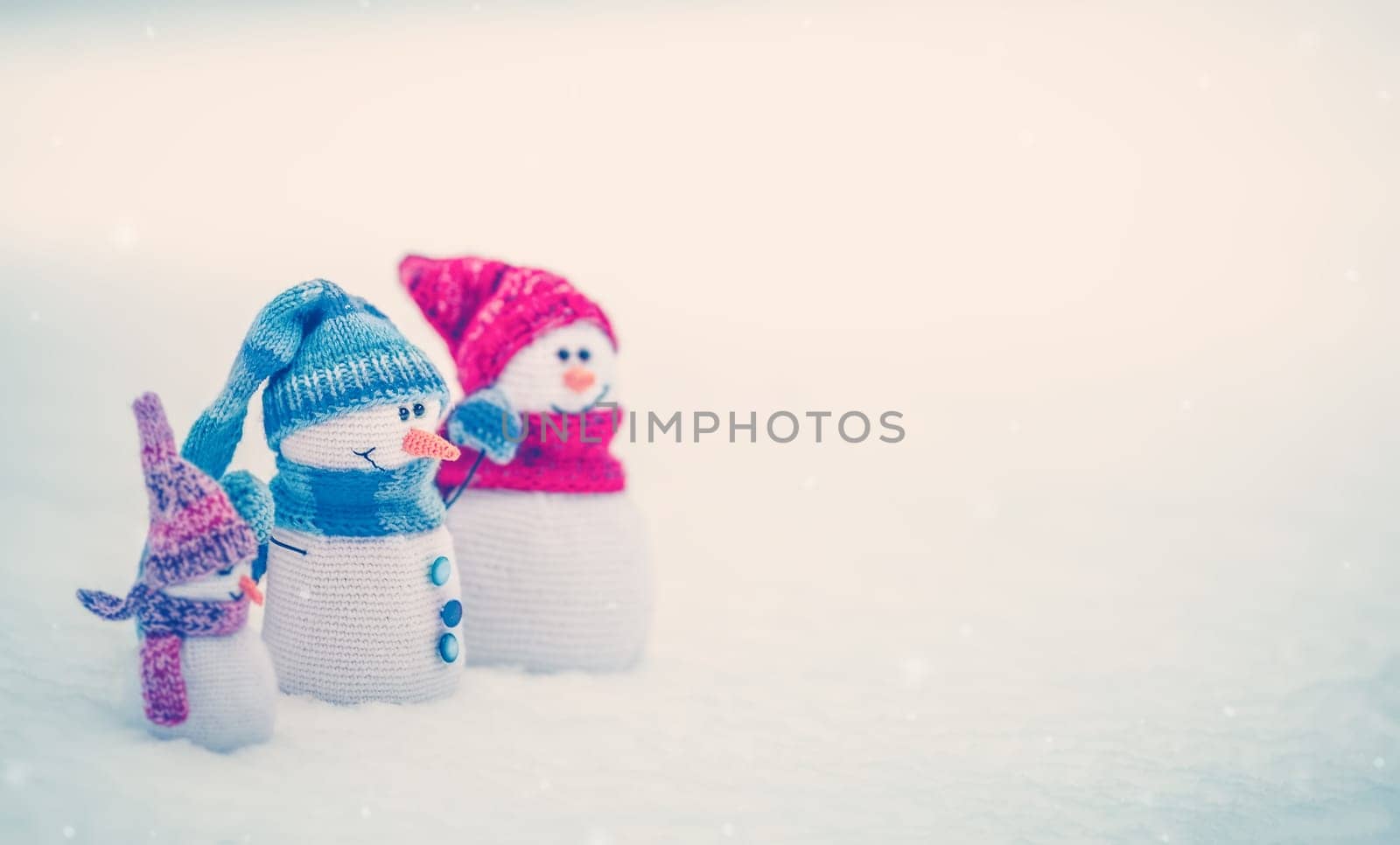 Little knitted snowmen on the white snow in nature. Concept of the wallpaper and greeting card.
