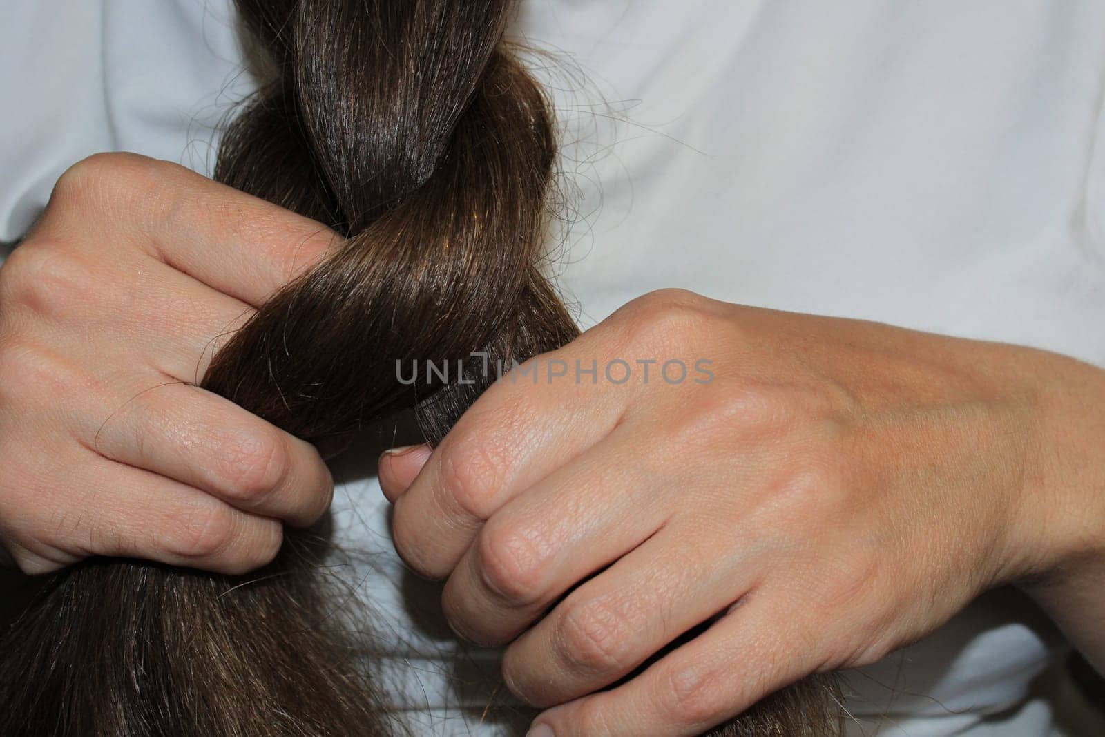 A girl with long dark hair is braiding her hair. Close-up hands. Hair care. Hair loss problem.
