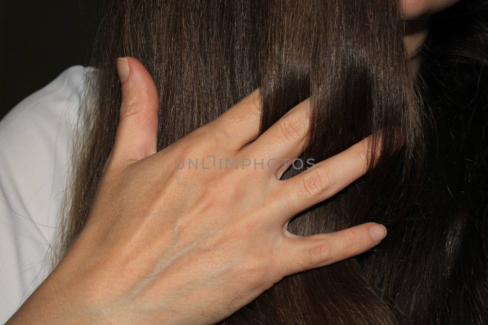 A girl with dark long hair put her hand through her hair. Hair care. Hair loss problem.