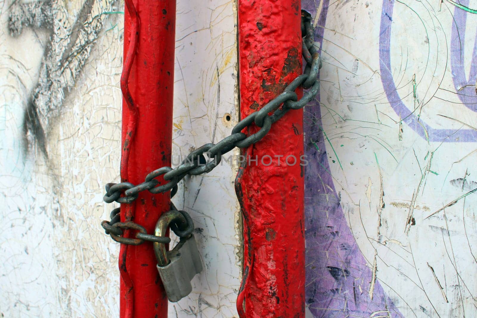 An old padlock on a rusty chain wrapped around red pipes.