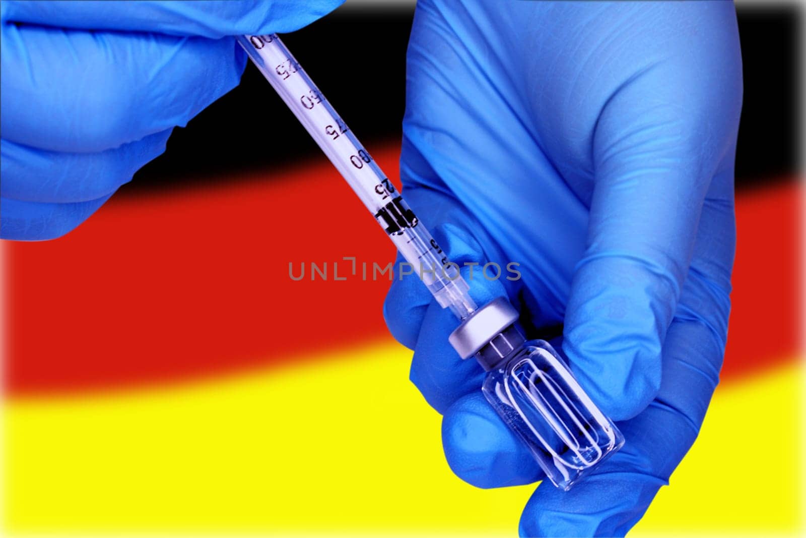Close-up hands in blue medical gloves draw a vaccine from a vial into a syringe against the background of the flag of Germany. Doctors strike concept.
