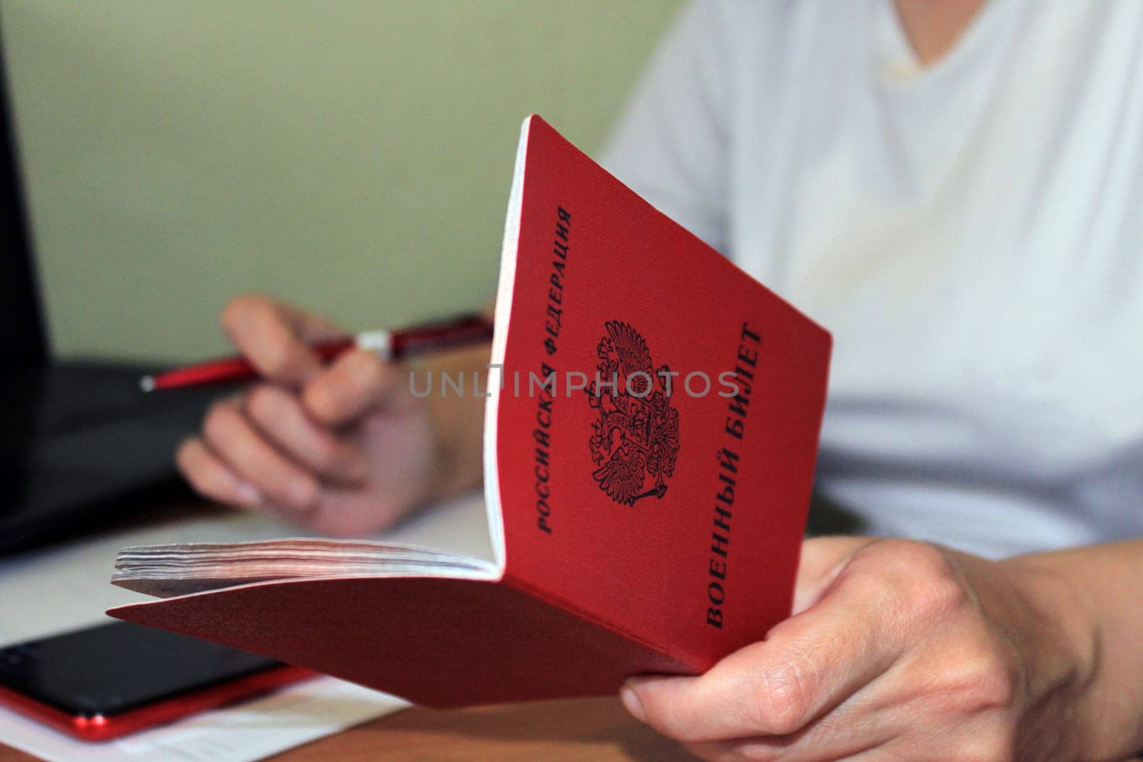 The girl holds a military ID issued by the Russian Federation in her hand and writes down his data. The concept of mobilization.