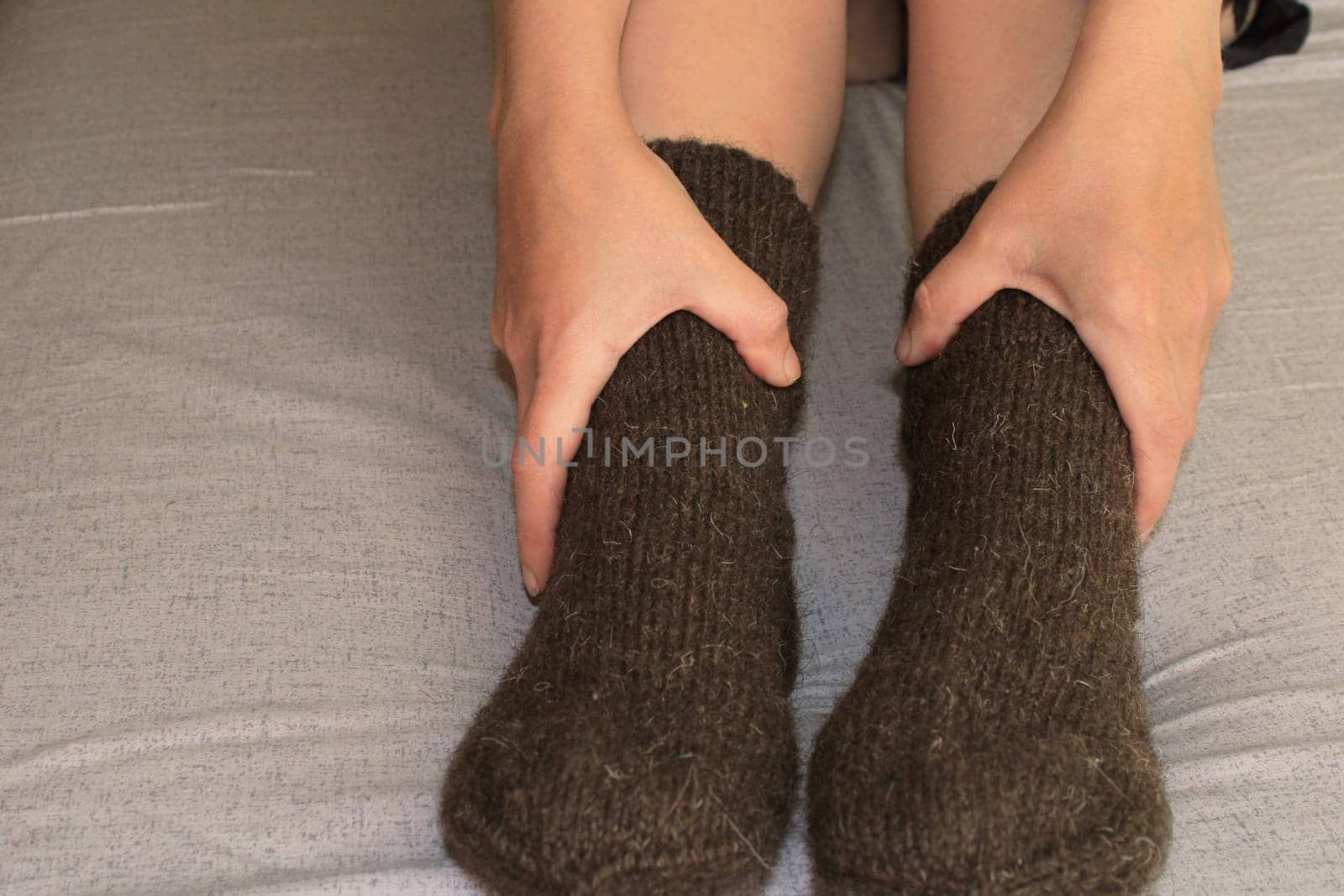 A young woman with slender legs sits on a bed at home in brown woolen socks. The concept of the world energy crisis.
