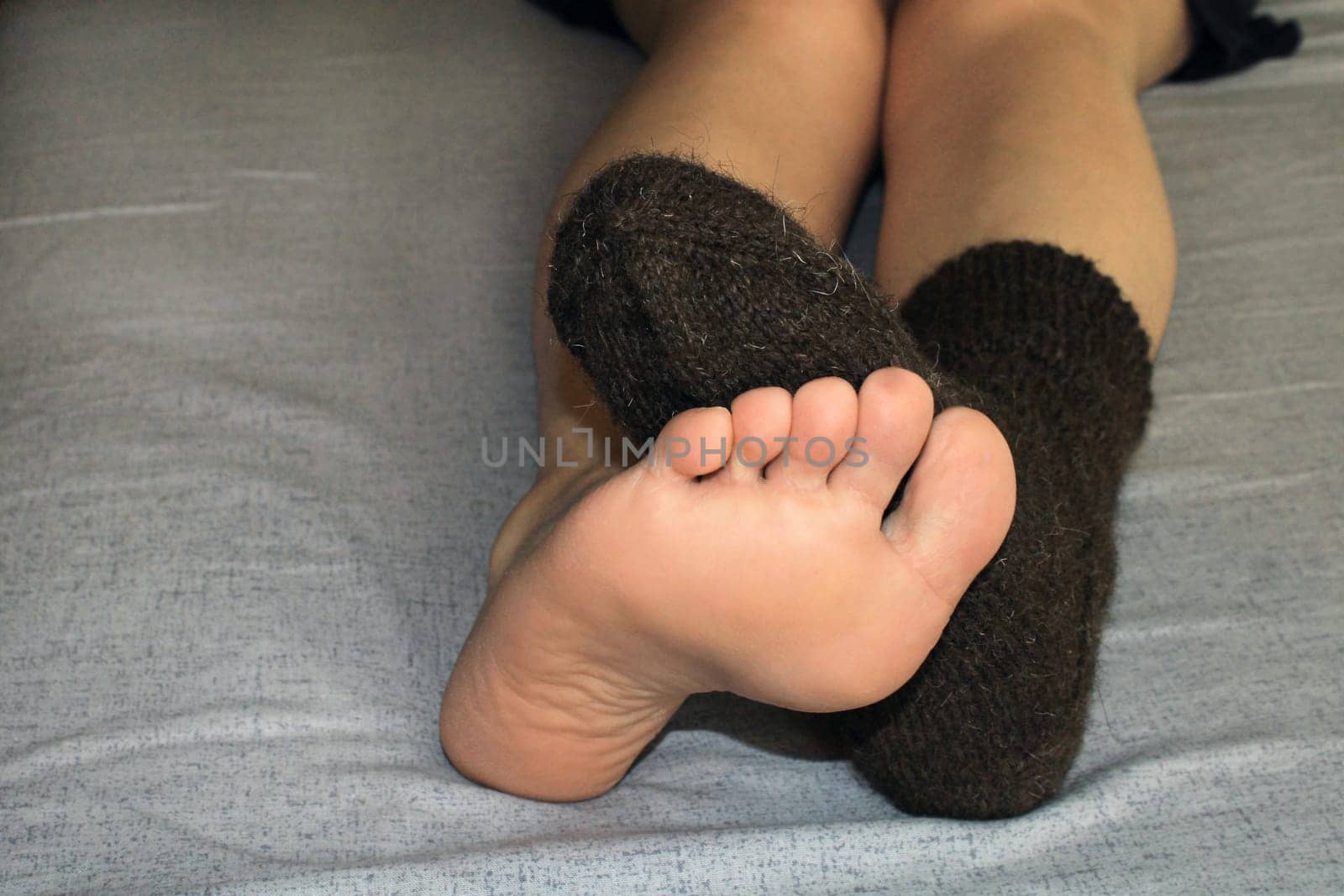 Two slender female legs close-up on the bed. One foot in a woolen sock, the other leg without a sock. The concept of the world energy crisis.