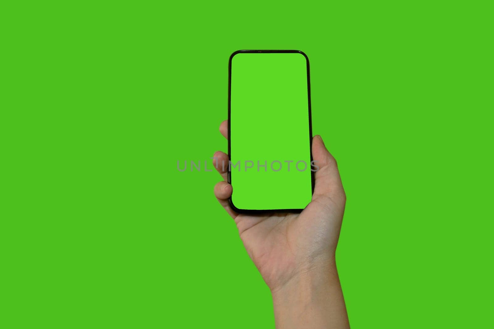 A woman's hand holds a smartphone with a green screen. Isolated object on a green background. Template for design. Mocap.