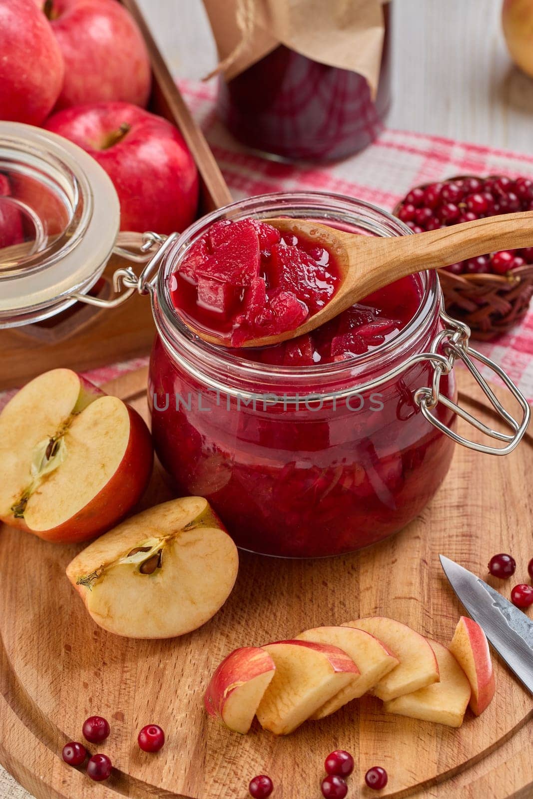 Wooden spoon with appetizing lingonberry and apple jam, jar of jam, fresh fruits and berries on light wooden table. Autumn harvest,  Home canning. Top view. Closeup