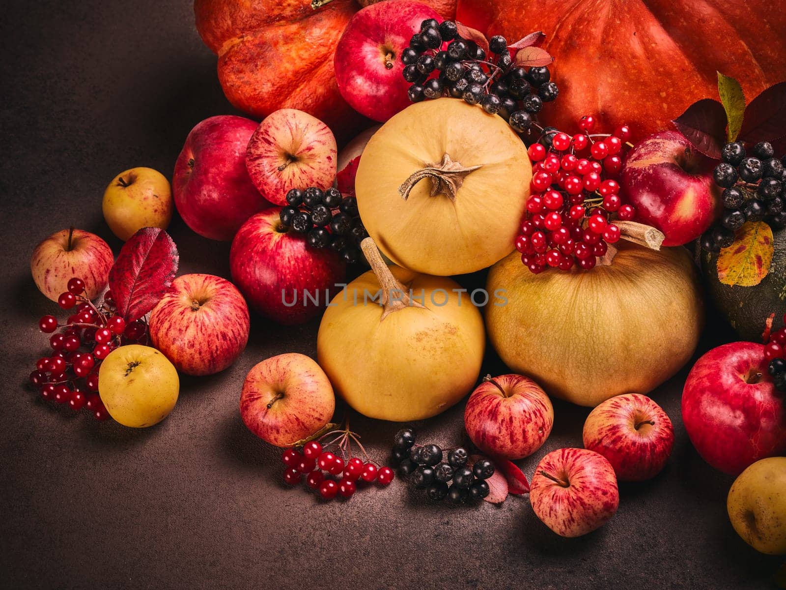 Thanksgiving background. Festive still life with pumpkins, berries, autumn leaves and apples on dark brown background. Happy Thanksgiving  day, autumn harvest, Halloween. Top view
