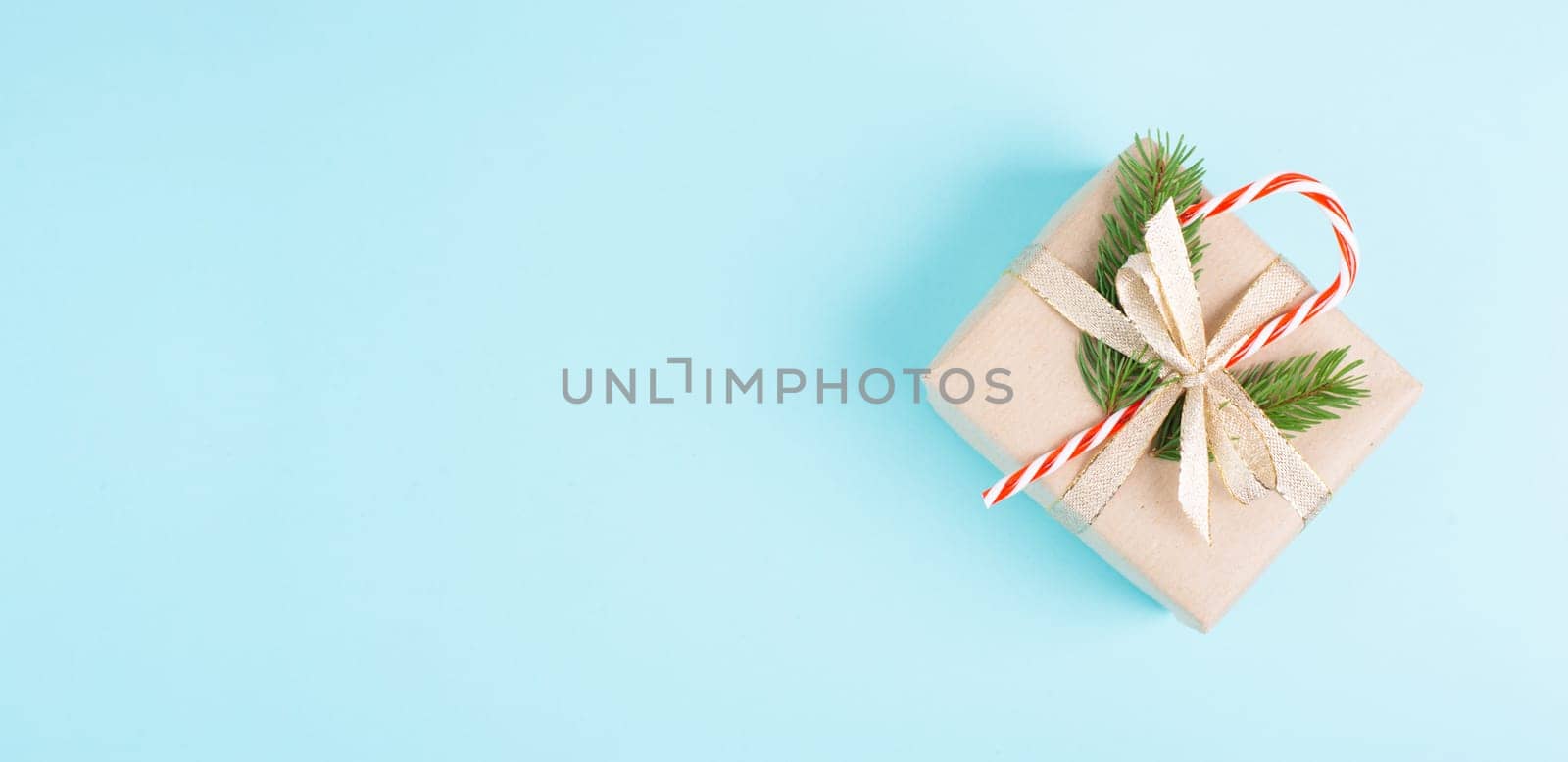 Christmas holiday greeting card with little gift box, candy cane, ribbon and fir branches, blue background