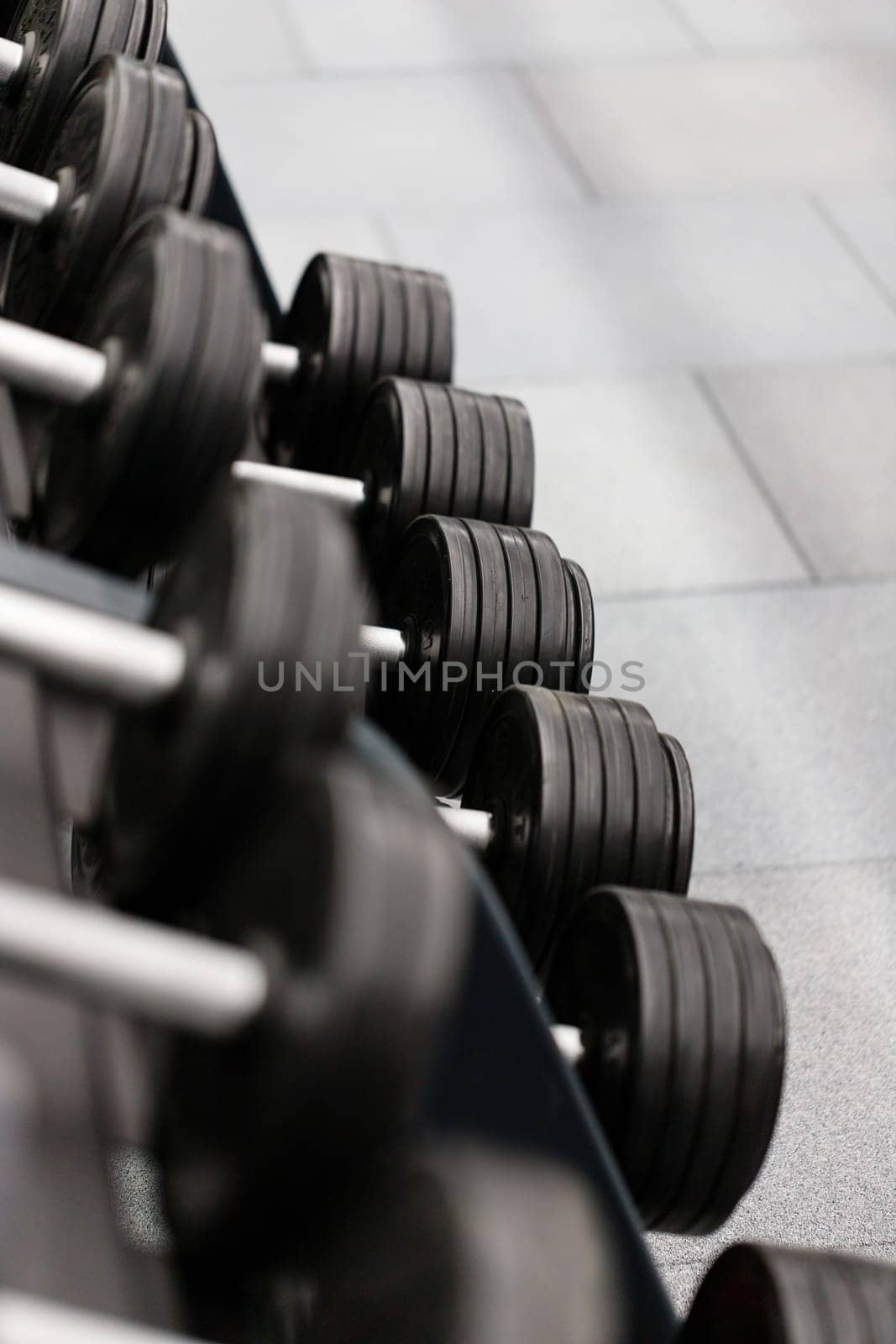Sport equipment and tool theme. Close up of gym equipment, black metal dumbbells lying in row on rack in modern sports complex. Sport concept. Selective focus.