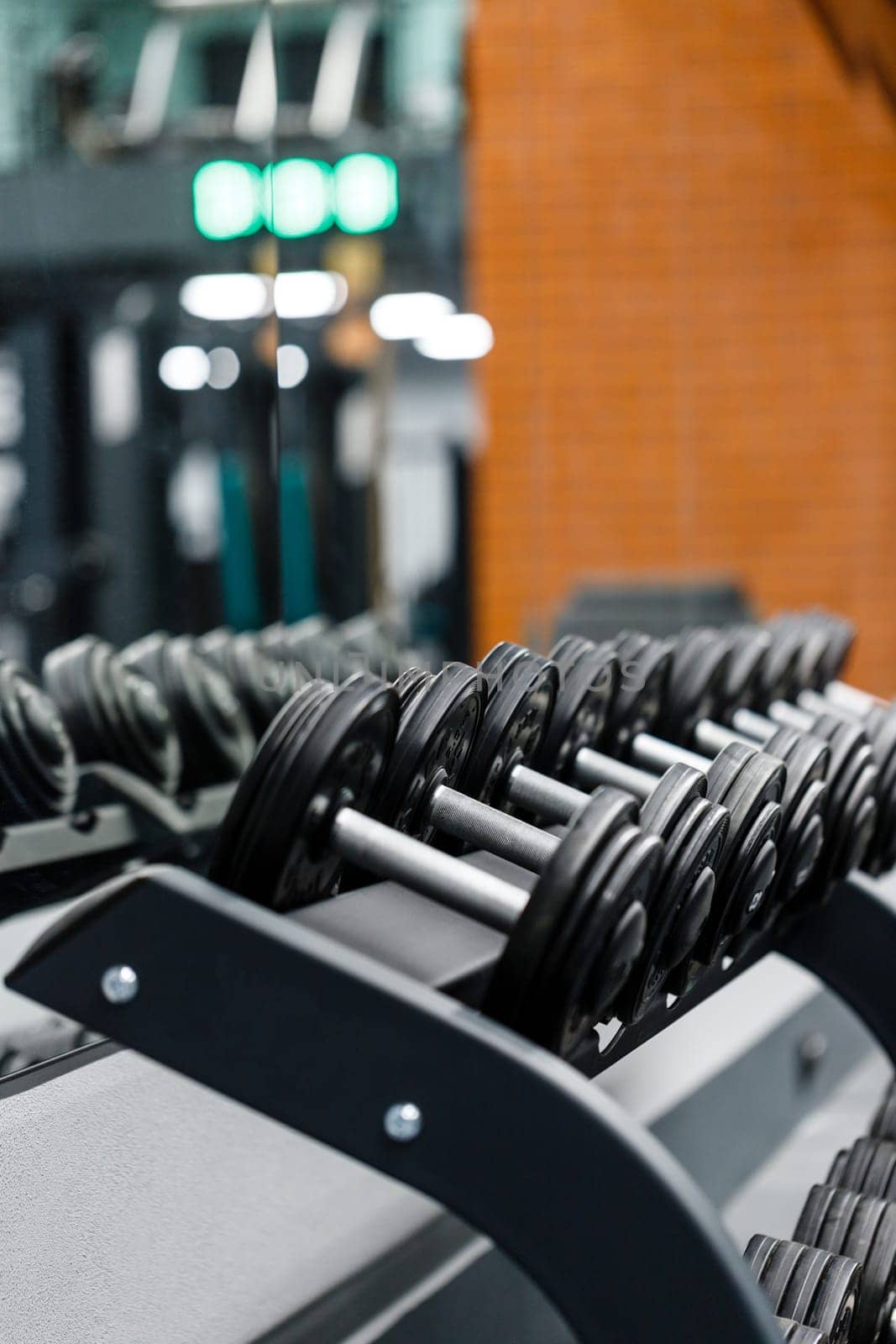 Close up set of dumbbells on black metal steel on rack in sports fitness center. Dumbbells in row are ready for use by athletes. Workout training and fitness gym concept.