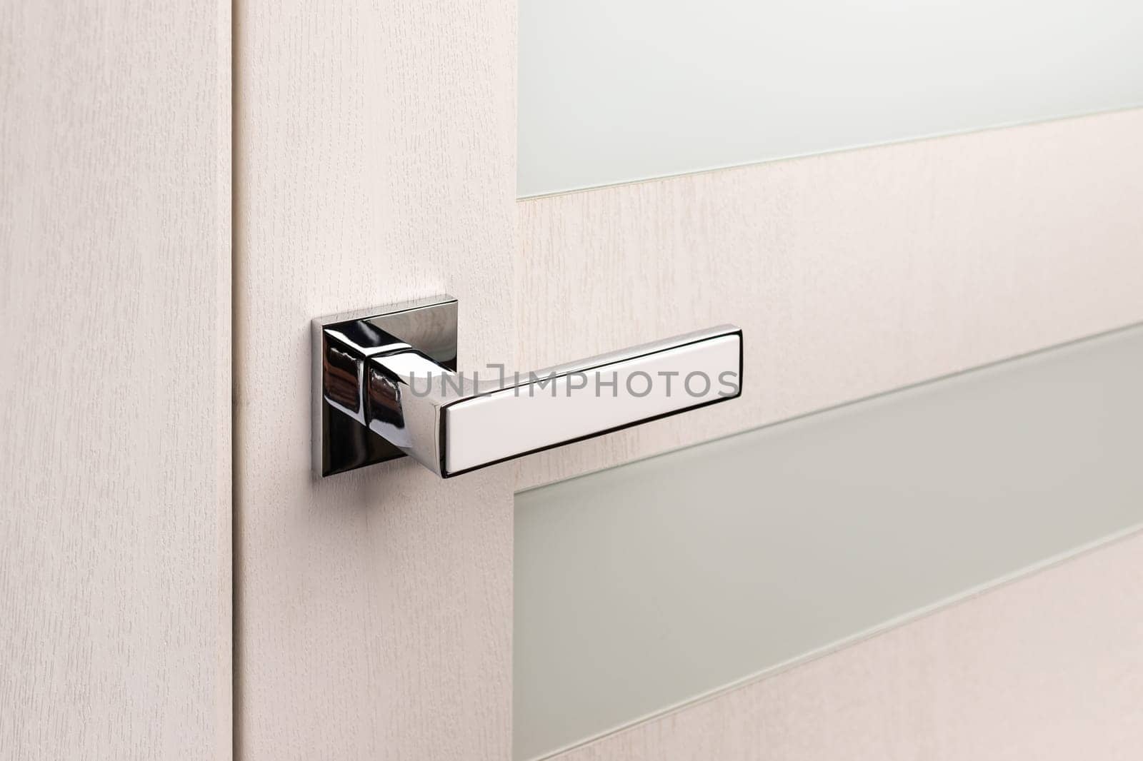 Close up of beautiful and stylish new metal door knob on modern interior door. Silver door handle with white insert on light beige door with frosted glass.