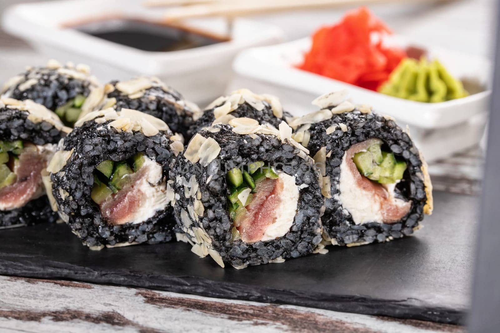 Close up of original unconventional sushi with black rice. Close up of pieces of sushi roll on black metal board.