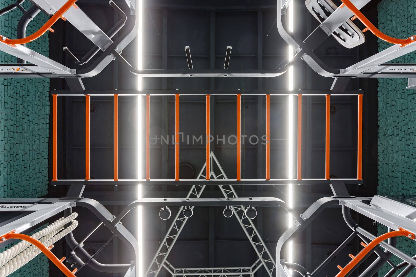 Sports background. Stylish modern interior gym with details from sports equipment. Bottom view of sports equipment bars and exercise machines in black and orange in sports complex with modern lighting