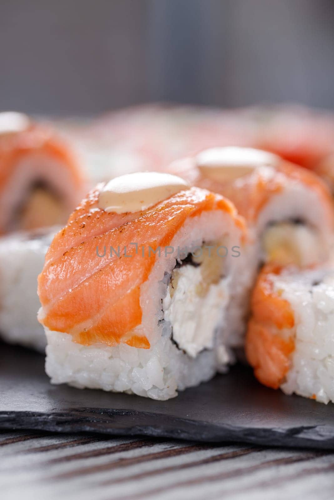 Popular food. Set of Philadelphia sushi on black concrete plate on table. Close up of pieces of sushi rolls with salmon on top and with cheese and eel inside.