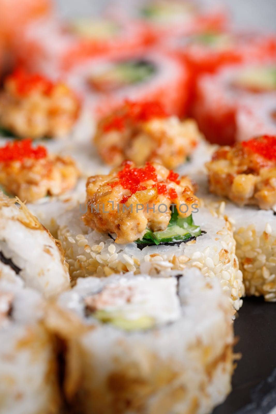 Traditional japanese sushi roll with tuna, tobiko red caviar and cucumber. Close up of piece of sushi covered with white sesame seeds and topped with minced tuna and red caviar and covering filling.