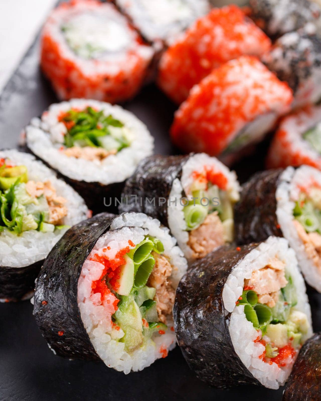 Asian cuisine. Large sushi set of various sushi rolls is served on black square metal slate. Side view of different rolls with variety of fresh ingredients.