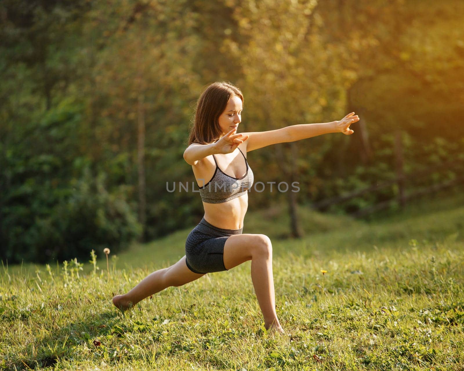 Yoga outdoor. Happy athletic woman with outstretched arms practicing breathing exercises and yoga standing barefoot on the grass. Yoga as a daily morning ritual.