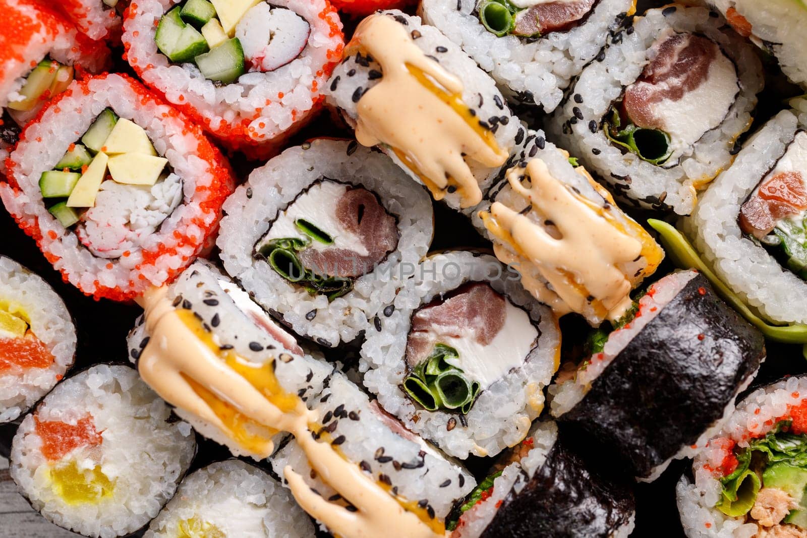 Close-up view of various sushi rolls with different fillings on black metal slate. Sushi set with salmon, red caviar, cheese, cucumber, avocado and sesame seeds. Sushi background.