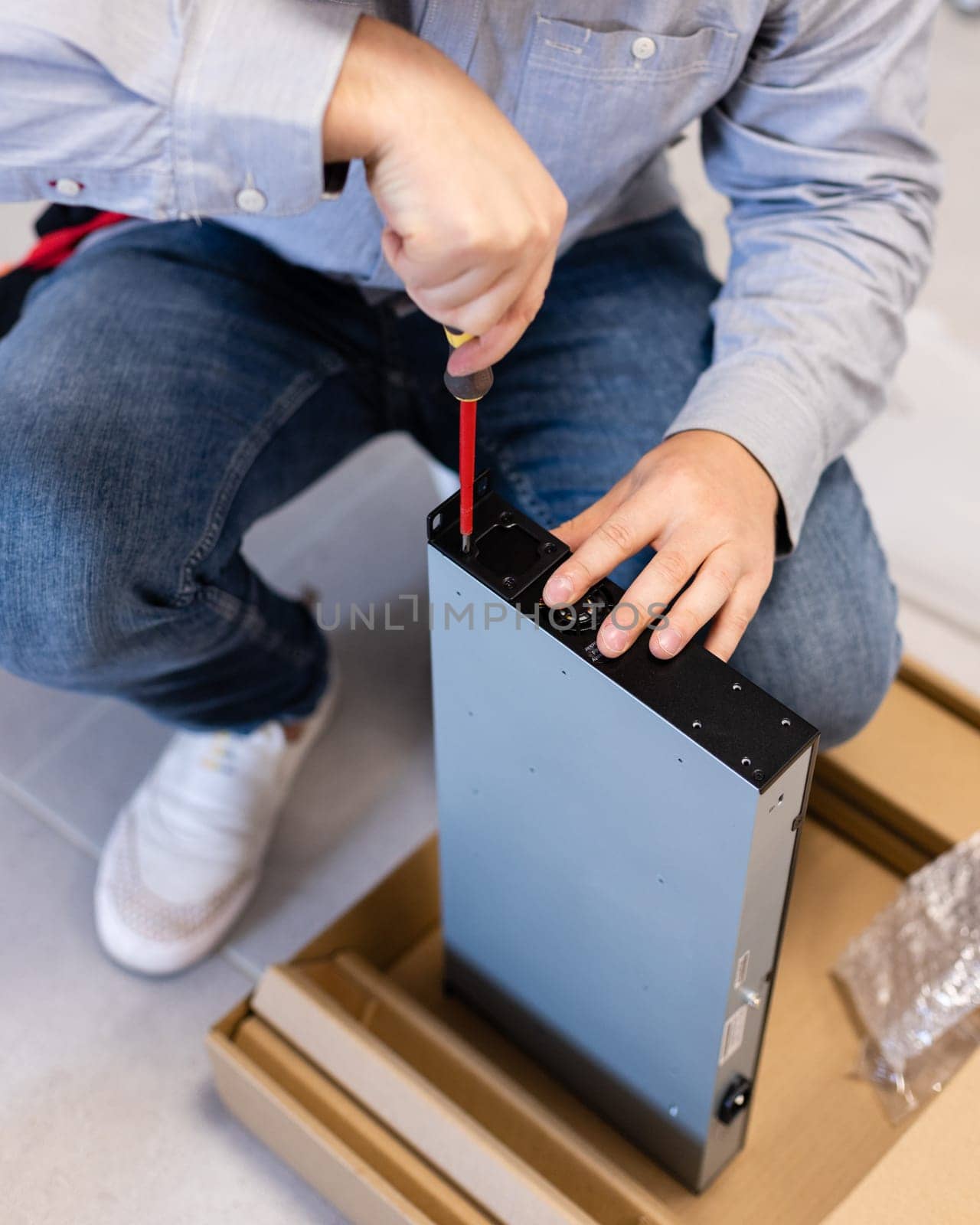 Computer specialist. Hardware installation and upgrades of modem system unit for Internet with help of screwdriver. Focused young male technician tightens screws in metal box of unit.