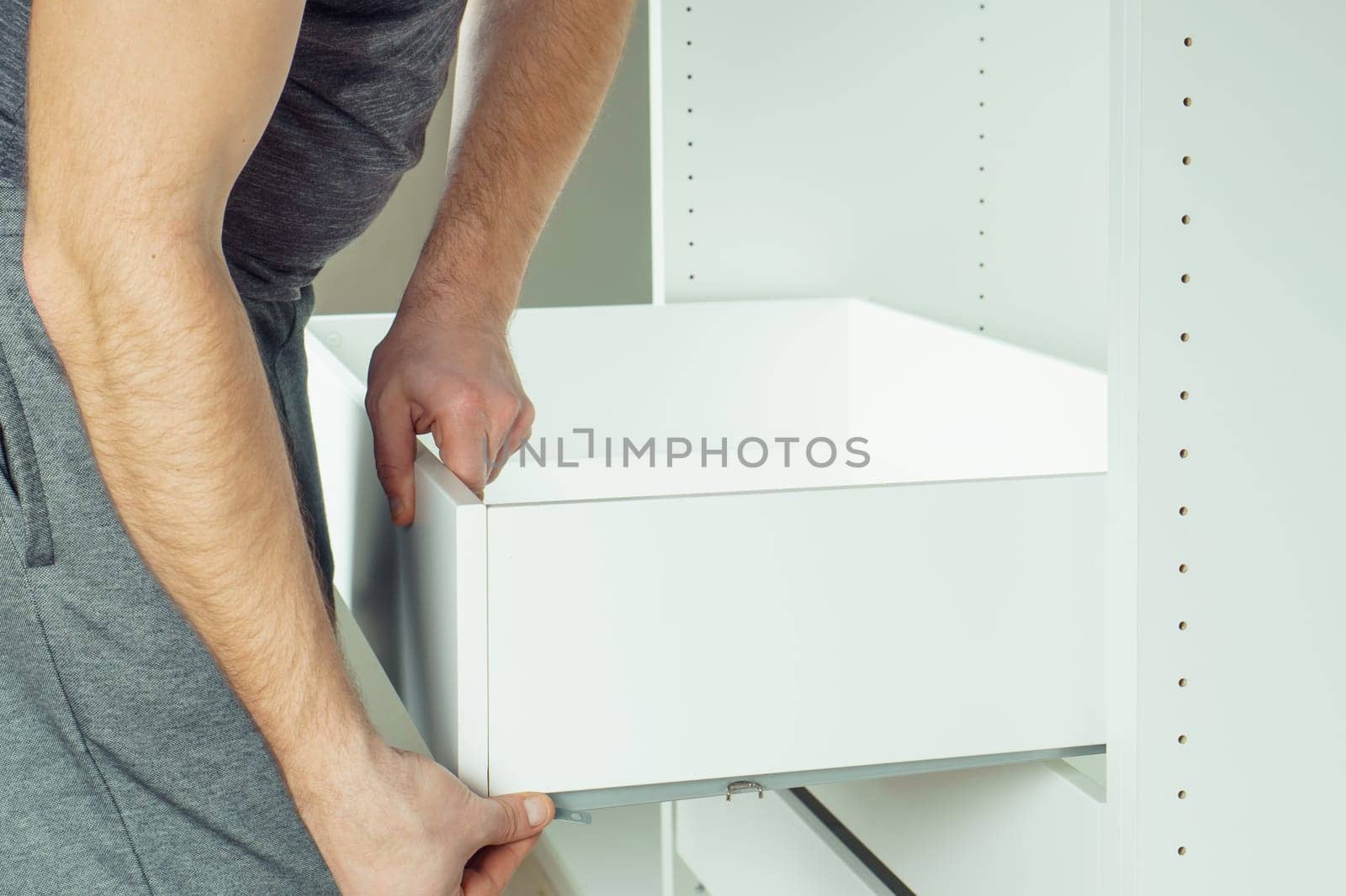 Male hold drawer, inserting and securing it to rails, assembling white dresser or wardrobe. Self-assembly of furniture at home, DIY, furniture repair and rearrangement