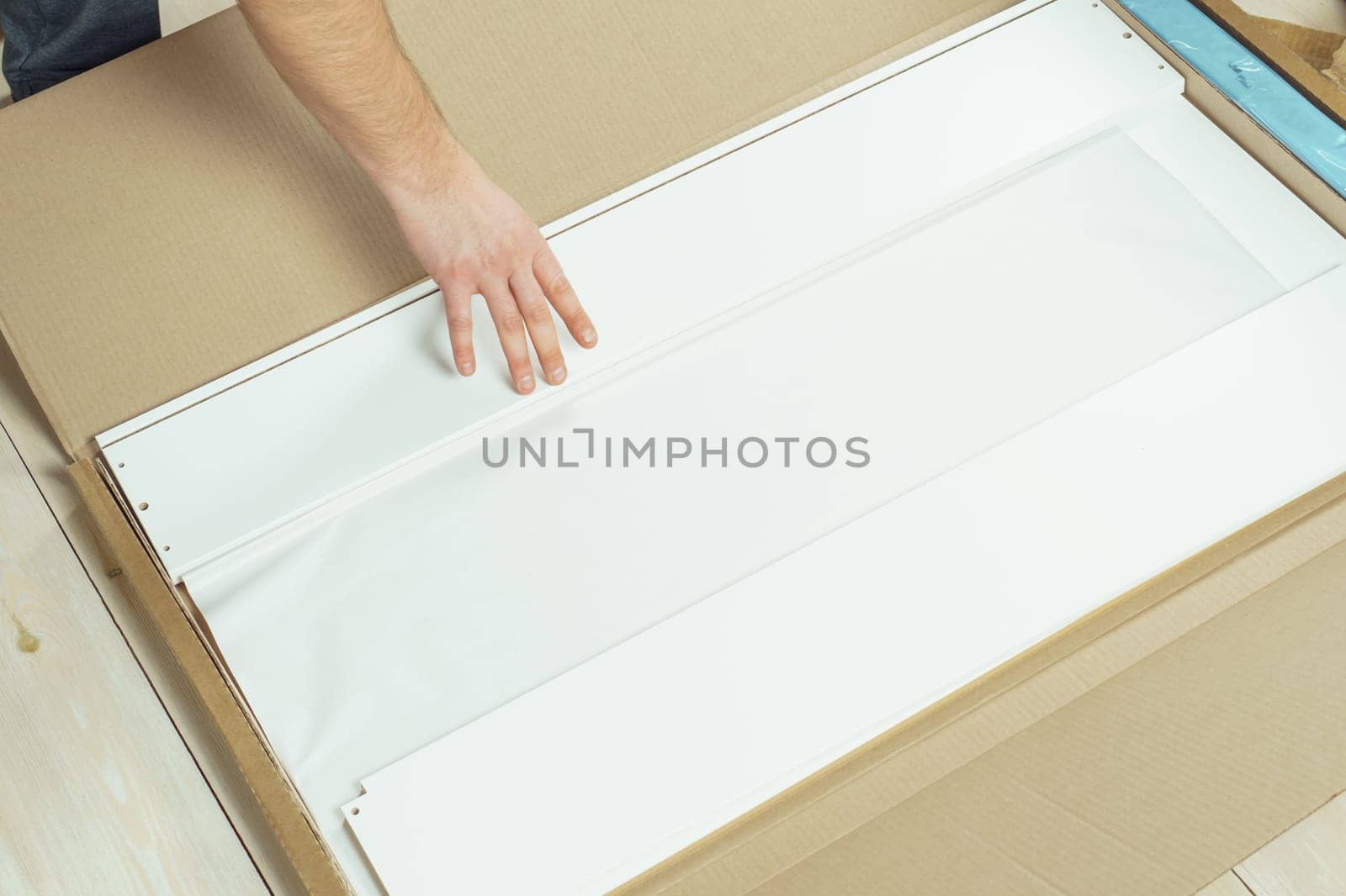 Male hands unpacking cardboard box with parts for assembling white chipboard drawer, dresser or wardrobe on floor. Self-assembly of furniture at home, DIY, furniture repair