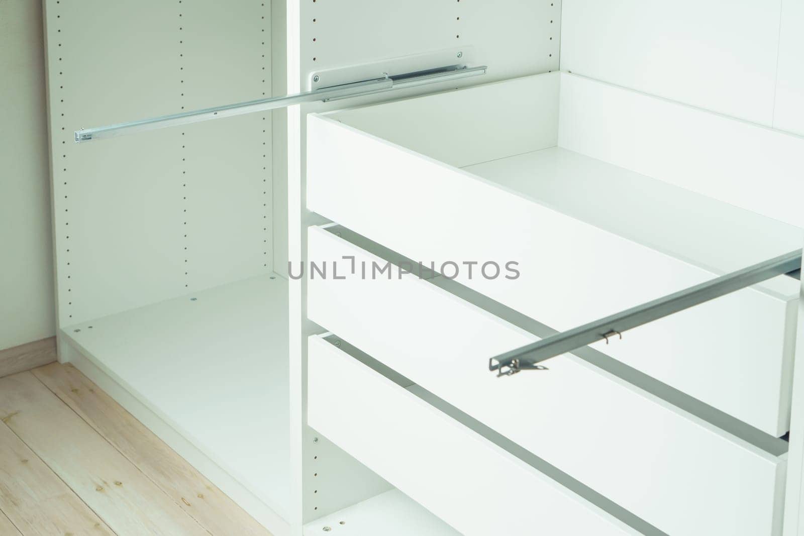 Drawer rail inserted into cabinet, fixed with self-tapping screws. Assembling white dresser or wardrobe. Self-assembly of furniture at home, DIY, furniture repair and rearrangement