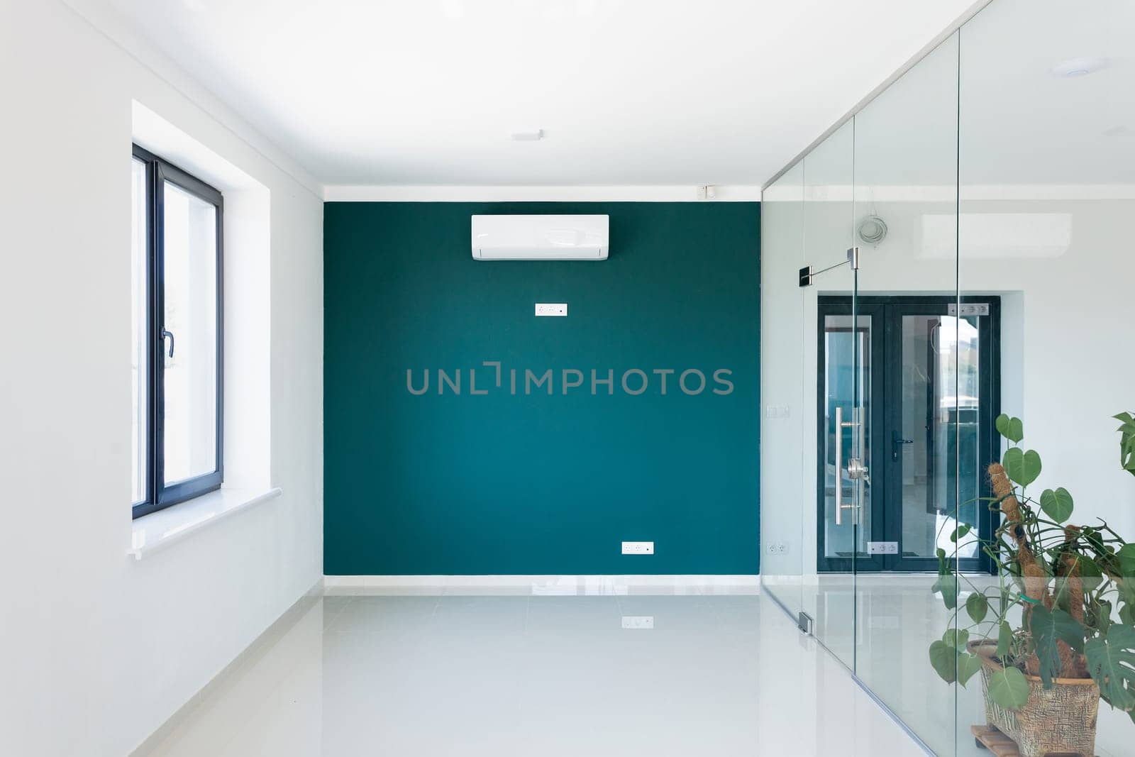 Stylish empty office interior with air conditioning on wall in modern business center. Green wall with air conditioning and sockets, white walls and glass doors in modern office space.