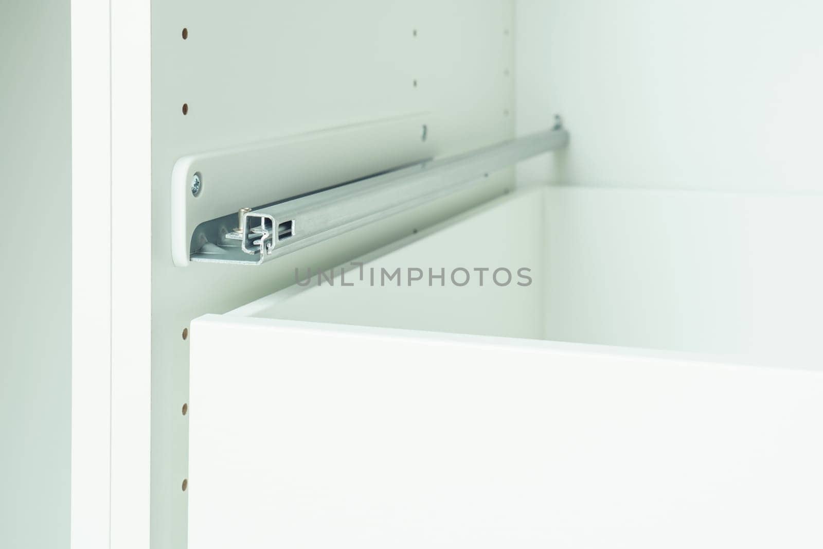 Drawer rail inserted into cabinet, fixed with self-tapping screws. Assembling white dresser or wardrobe. Self-assembly of furniture at home, DIY, furniture repair and rearrangement