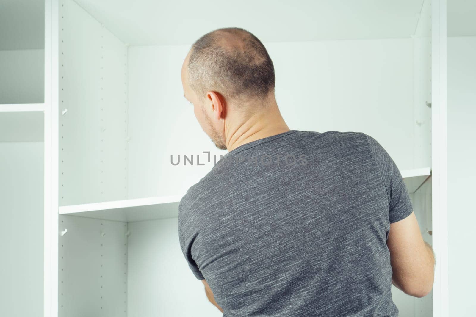 Male hold shelf, inserting and securing it to supports, assembling white dresser or wardrobe. Self-assembly of furniture at home, DIY, furniture repair and rearrangement