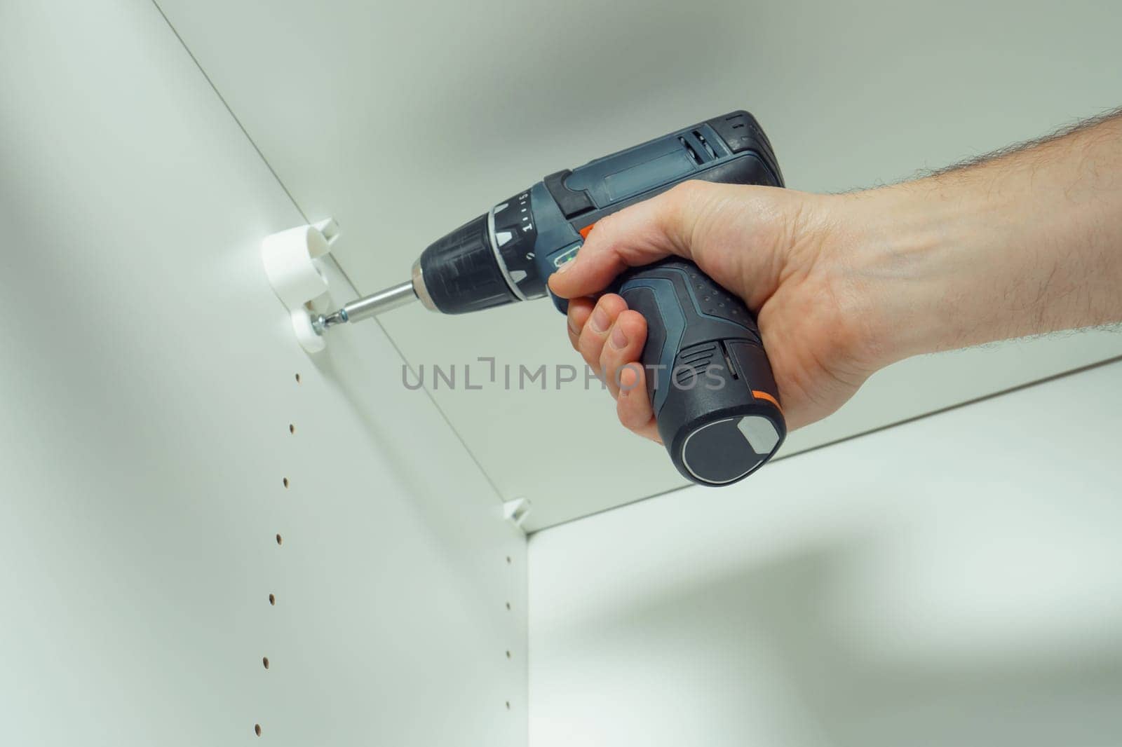 Male hands screw in to insert plastic support into one of series of holes to fix white hanger bar, assembling dresser or wardrobe. Holds screwdriver. Self-assembly of furniture, DIY, renovation