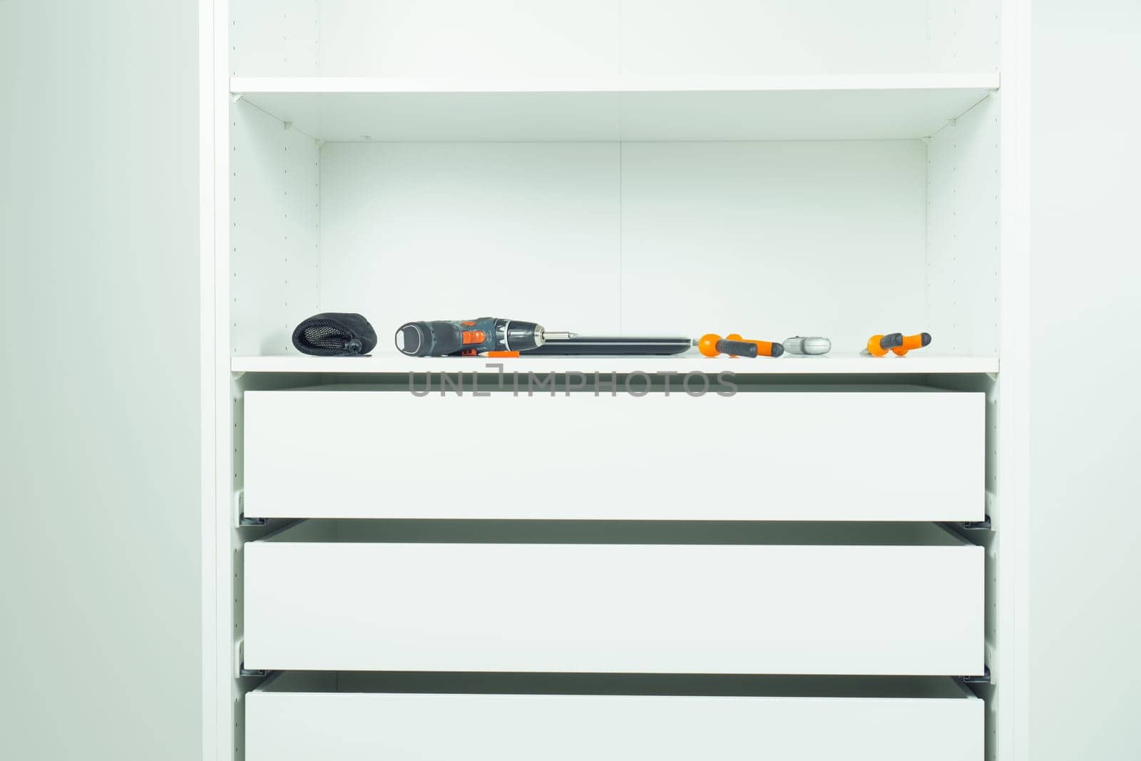 Inserted and fixed cabinet drawers and shelves. Assembling white dresser or wardrobe. Tools lie on shelf - screwdriver, pliers, knife, pencil. Self-assembly of furniture at home, DIY, furniture repair