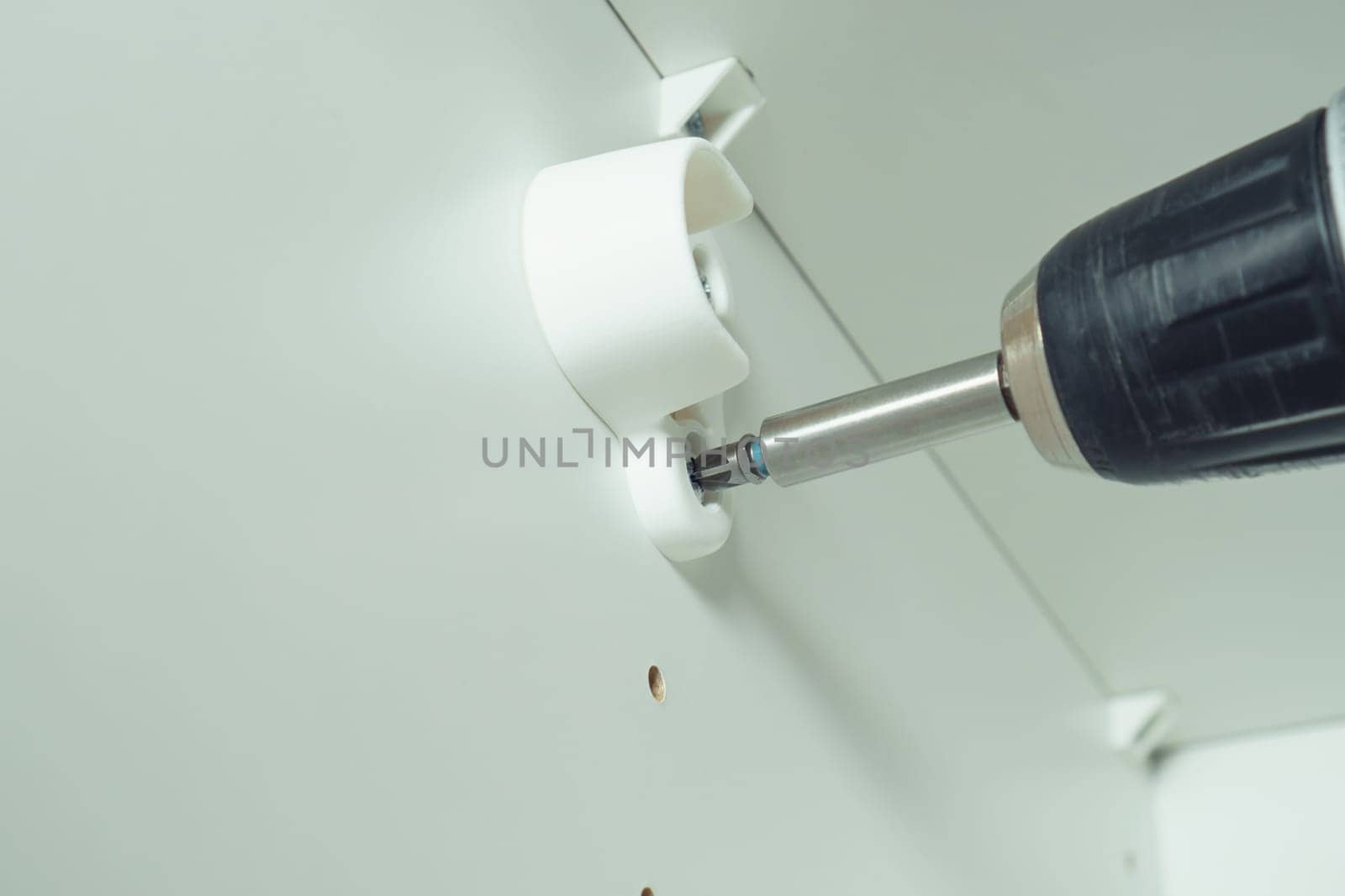 Closeup of screw in to insert plastic support into one of series of holes to fix white hanger bar, assembling dresser or wardrobe. Screwdriver. Self-assembly of furniture, DIY, renovation