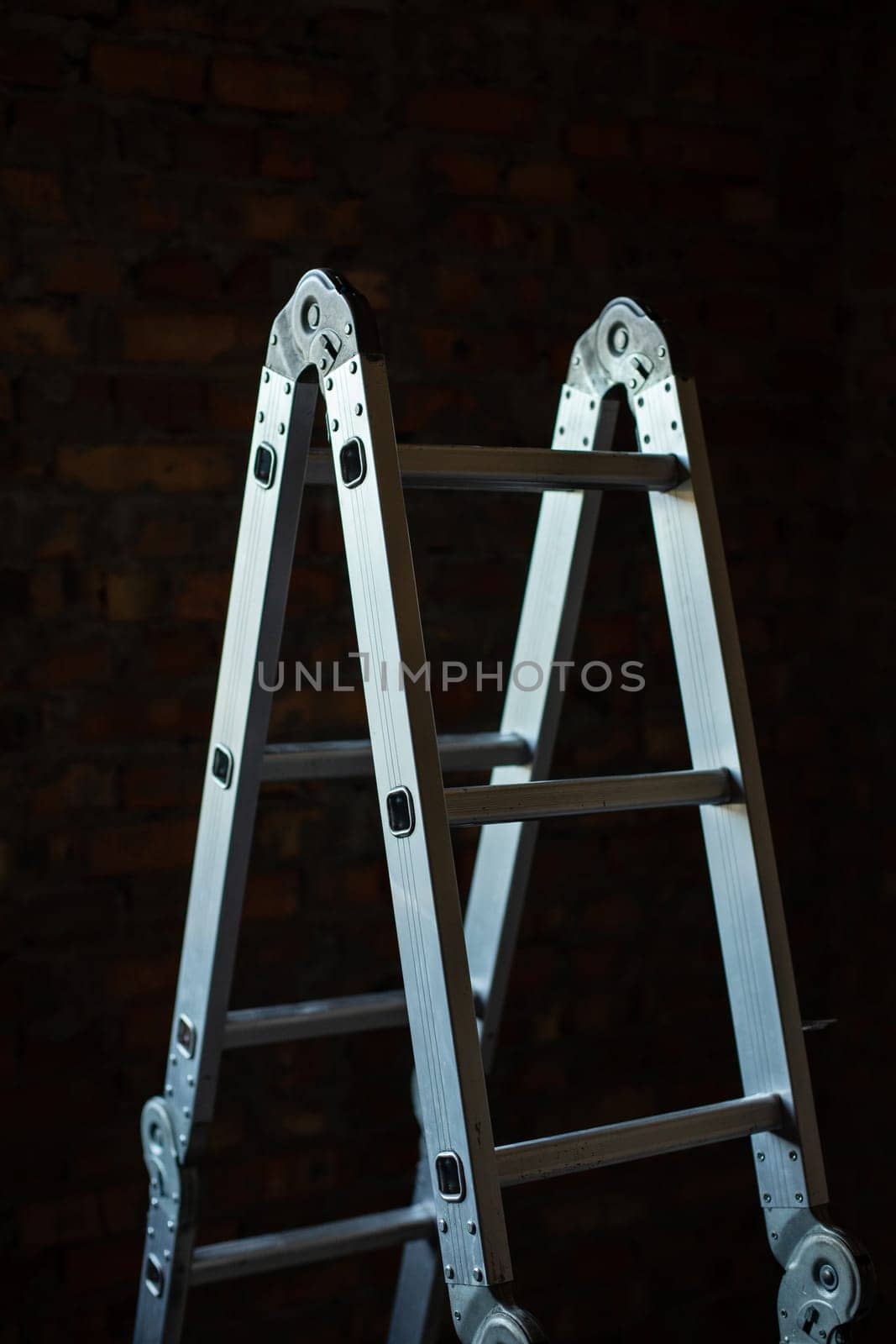 Construction. Metal folding step ladder in a dark room on a construction site. Close up of new construction step ladder on brick wall background.