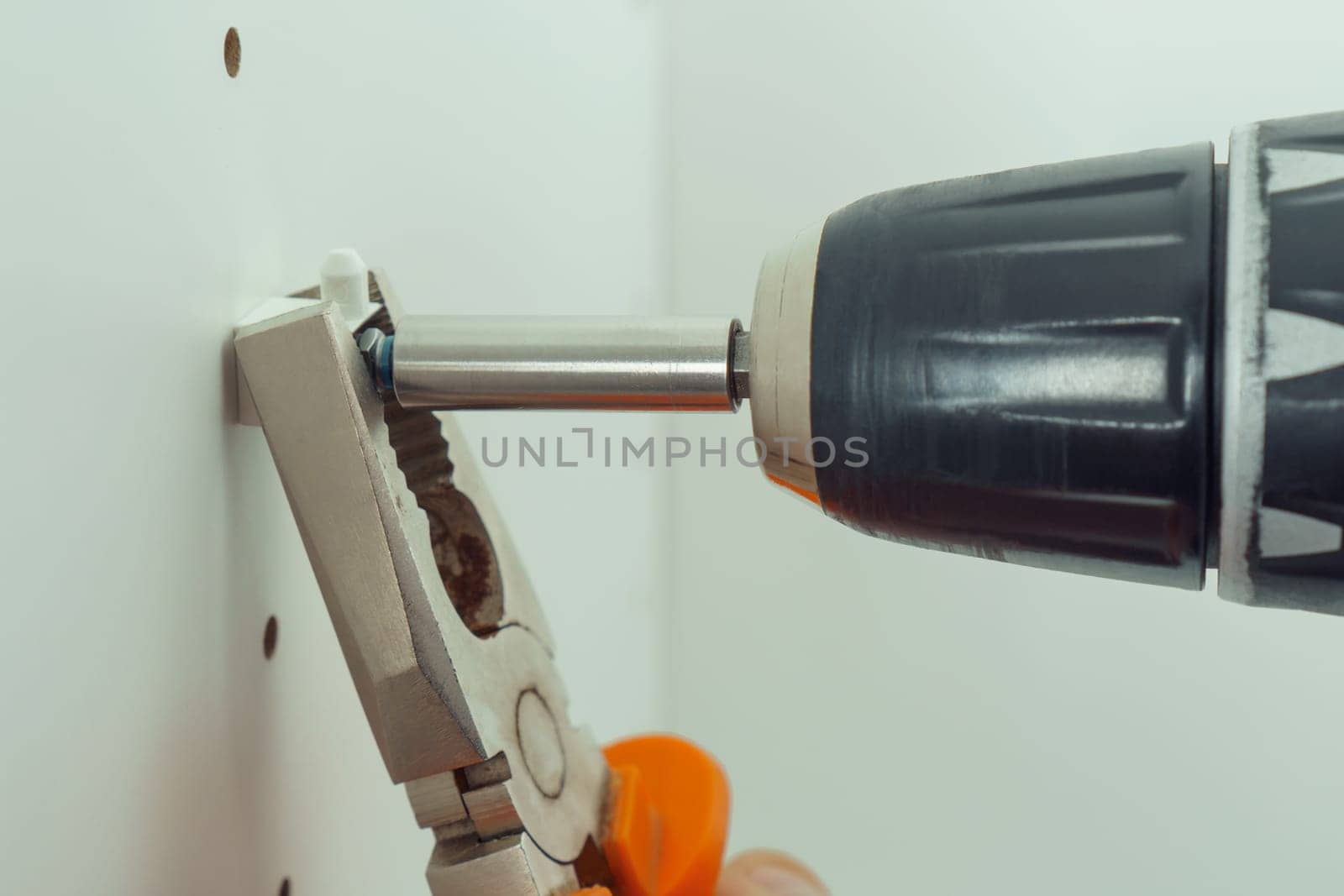 Closeup of screw to insert plastic support into one of series of holes to fix white shelf, assembling dresser or wardrobe. Holding screwdriver with pliers. Self-assembly of furniture, DIY, renovation