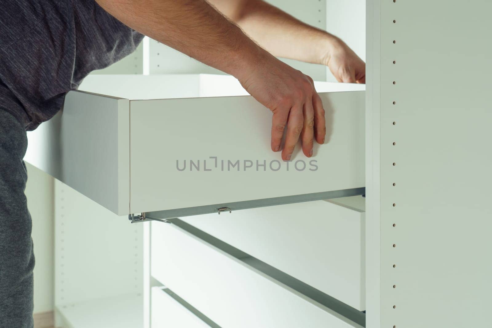 Male hold drawer, inserting and securing it to rails, assembling white dresser or wardrobe. Self-assembly of furniture at home, DIY, furniture repair and rearrangement