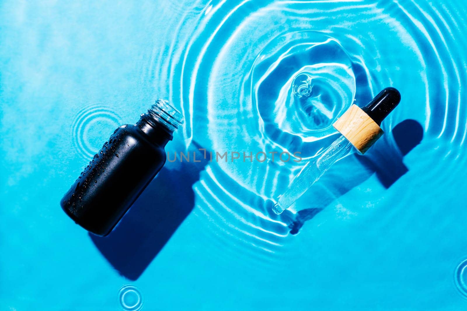 Facial pipette serum, essence cosmetic product in water drop splashing fresh transparent, flecks. Flat lay, top view. Summer beach tropical, vacation. Organic skin body anti age care in hot climate