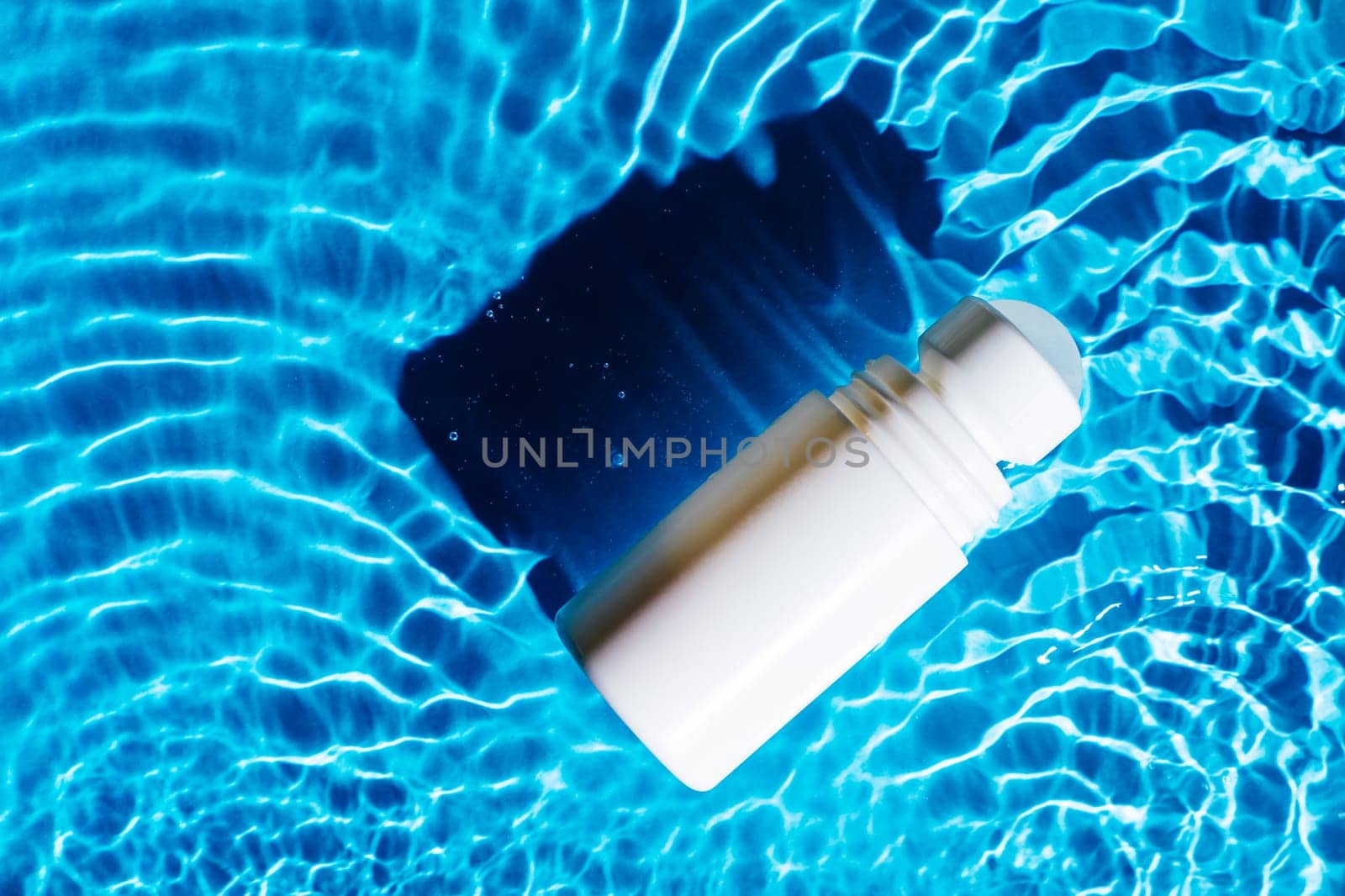 White beauty product roll on antiperspirant deodorant anti sweat smell, vial in transparent fresh water with flecks and waves, dark shade. Skin care protection in hot summer beach. Flat lay.