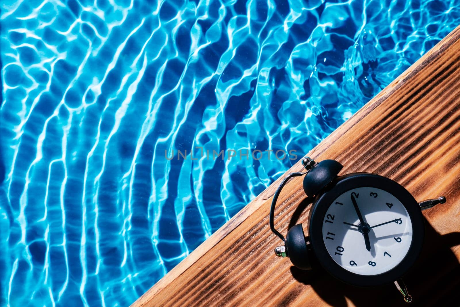 Wood sand board black alarm daily clock. Blue transparent reflect wave water surface ocean. Time aging running out. Vacation summer health care concept. Countdown youth. Flat lay, place for text.