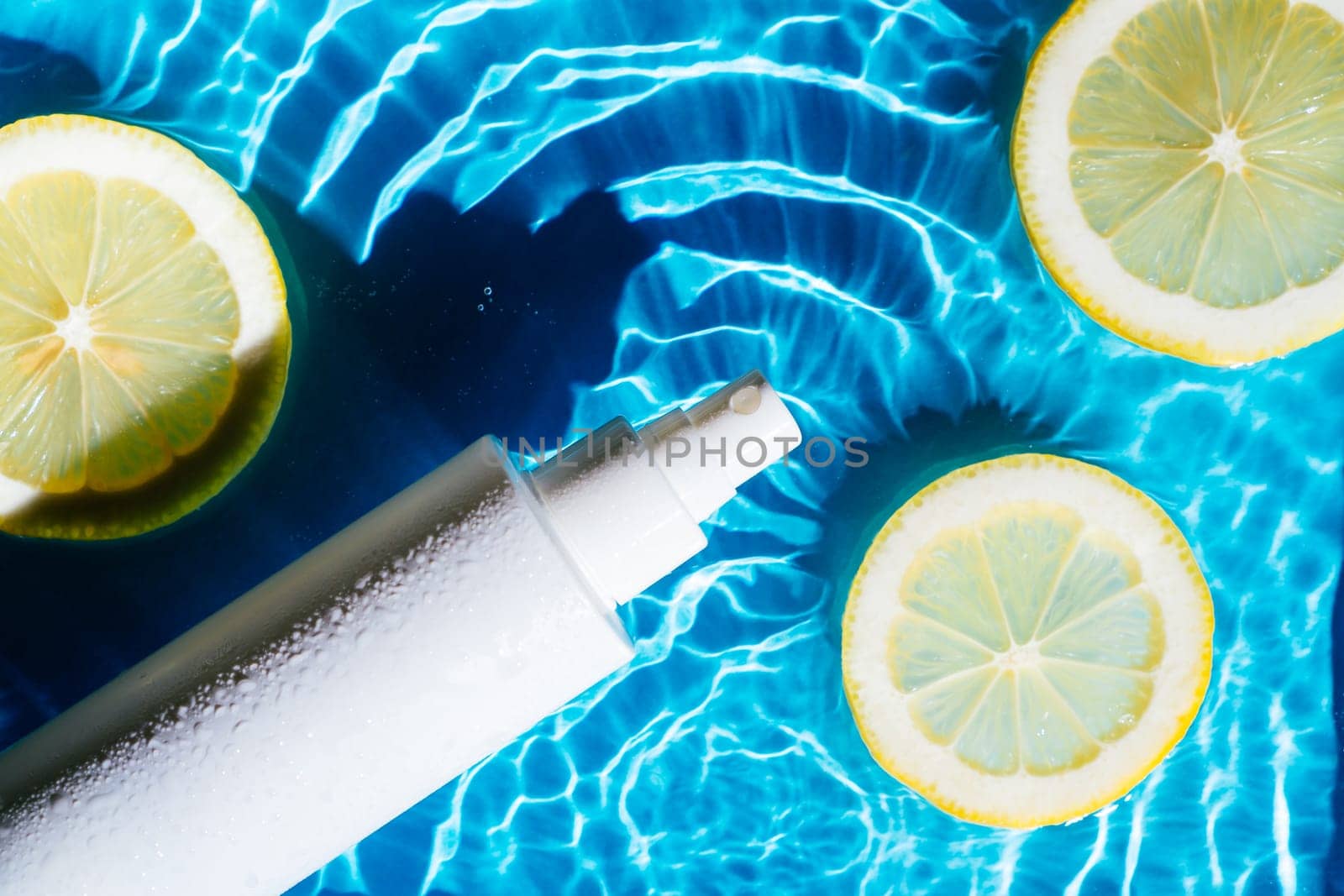 White beauty product sunscreen cream vial sprayer in transparent fresh water with flecks and waves, lemon citrus. Body skin care protection sunblock in summer beach travel concept. Flat lay.