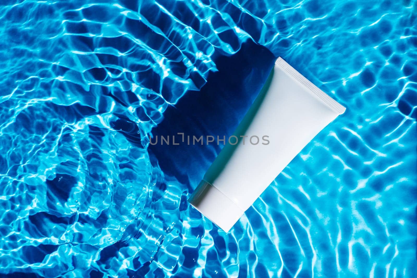 White beauty product sunscreen cream vial tube bottle in transparent fresh water with flecks and waves, dark shade. Body skin care protection in hot summer beach. Flat lay.