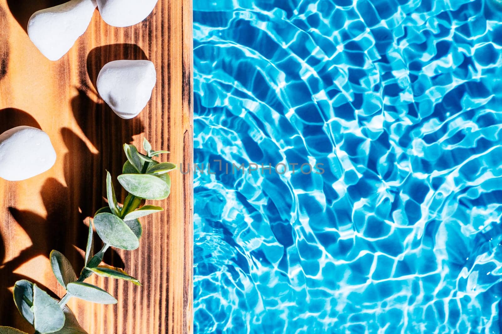 Wood sand board with hot white salt stones and twig natural eucalyptus. Blue transparent reflect wave water surface ocean. Hot warm stone massage therapy treatment concept. Right place for text.